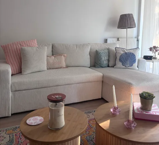 Aménagement d'un salon chaleureux avec canapé d'angle beige, tables basses en bois et décoration douce aux tons pastel.