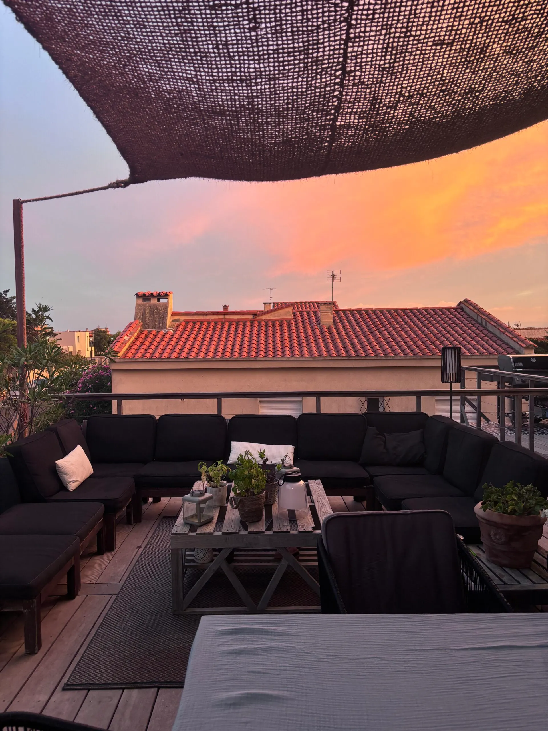 Terrasse avec grand canapé d'angle noir sous un voile d'ombrage.