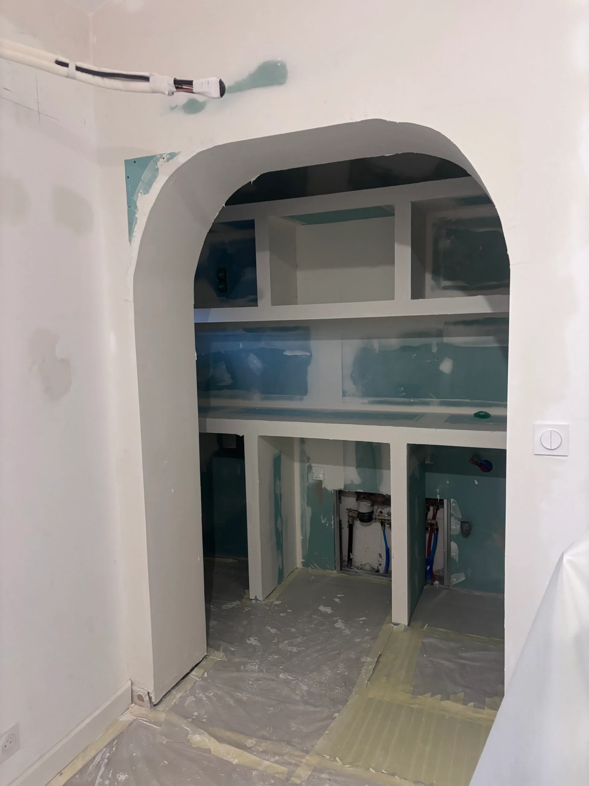Chantier d'aménagement d'une niche arquée sur mesure avec étagères intégrées, démontrant le travail de structure.