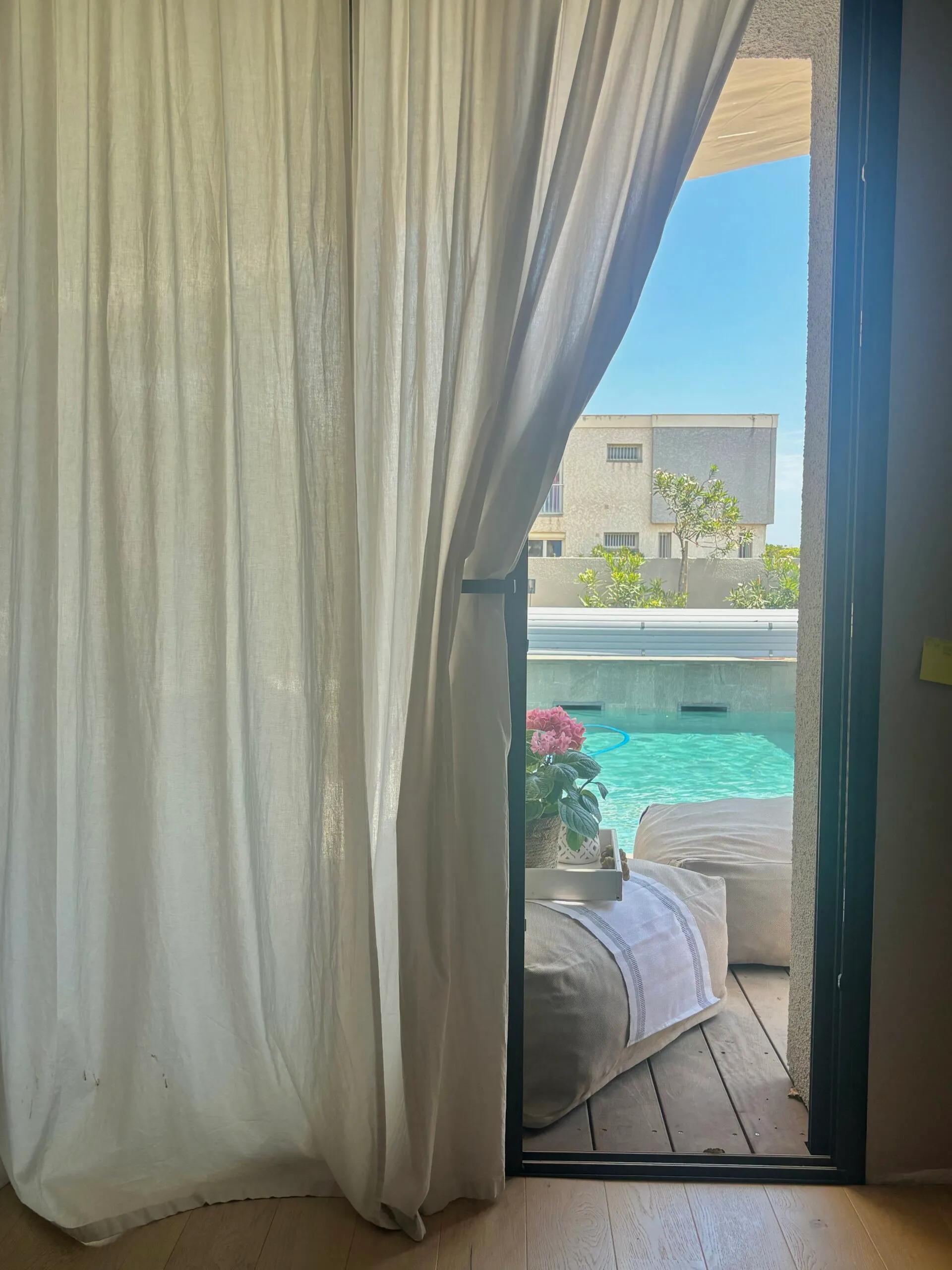 ue sur piscine depuis une chambre grâce à de grandes baies vitrées et des voilages légers pour une transition intérieur-extérieur fluide.