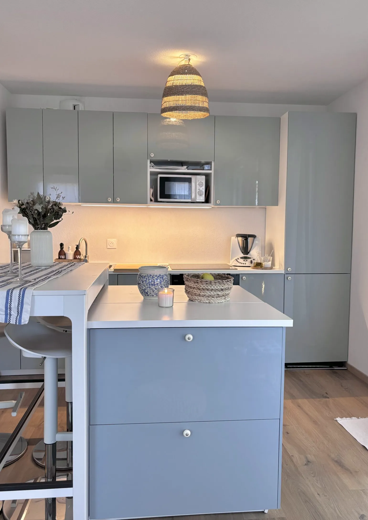 Cuisine ouverte moderne avec îlot central bleu gris et rangements fonctionnels.