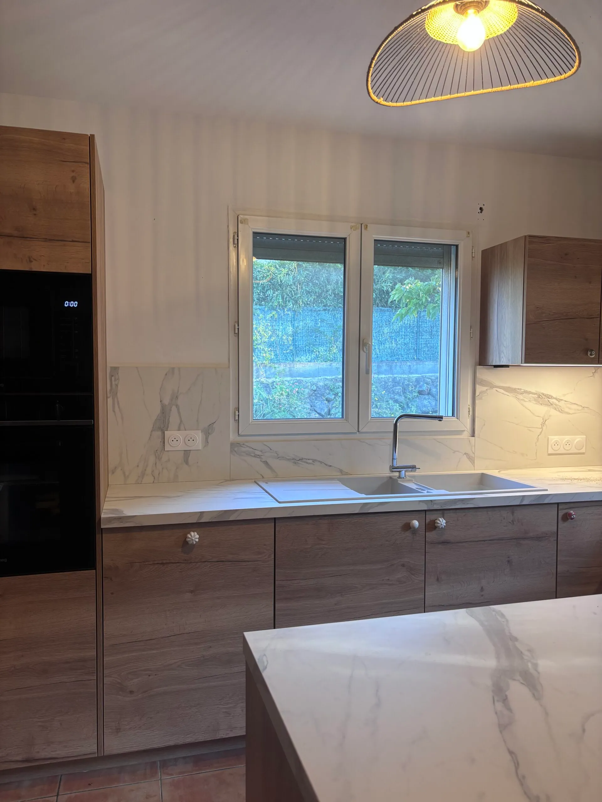 Cuisine moderne avec meubles en bois et plan de travail blanc.