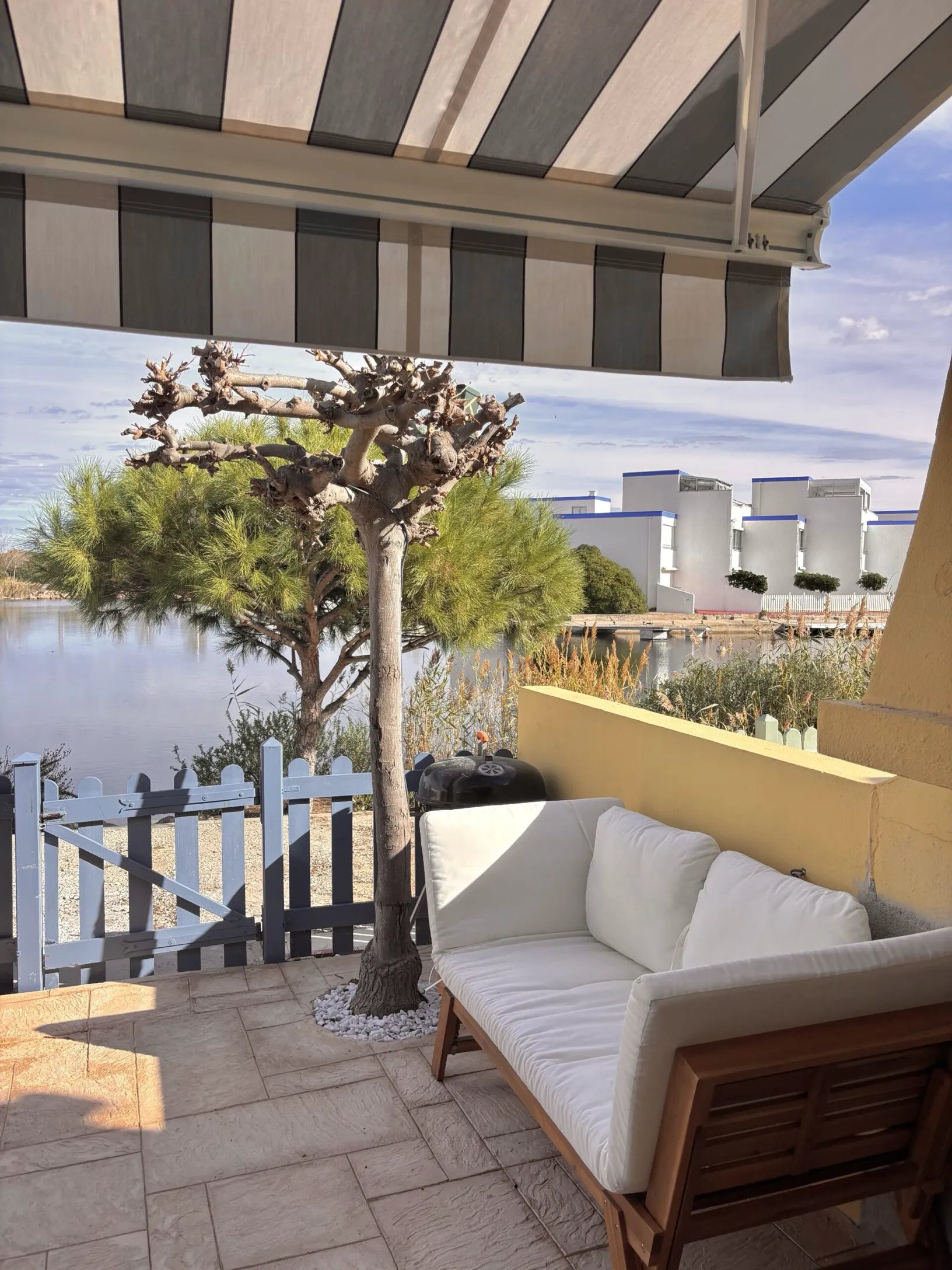 Aménagement de balcon avec mobilier de jardin blanc, store banne et vue dégagée sur les pins.